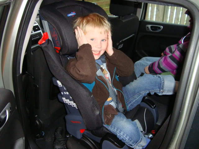 A young boy sitting in a car seat holding a cell phone - Pistonheads
