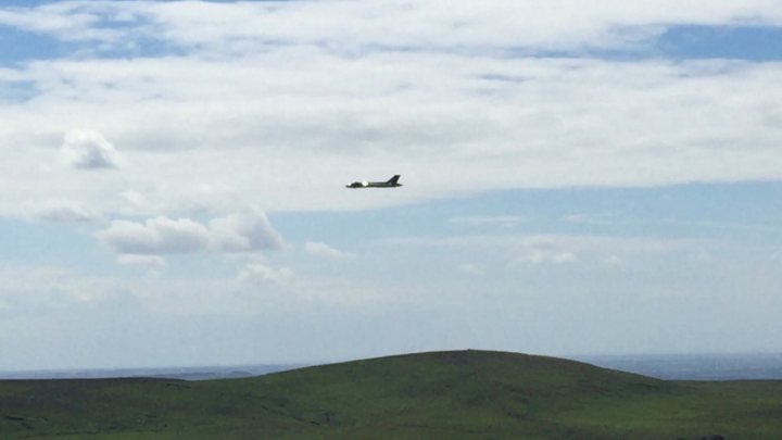 A plane flying over a field with mountains in the background - Pistonheads