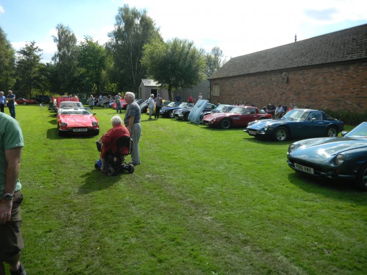 A group of people sitting on top of a lush green field - Pistonheads