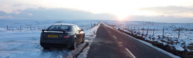 Today Vxr Pistonheads - The image showcases a serene winter landscape with a solitary car resting at the foot of a steep road heading towards a vanishing point. The snow-covered road reflects the soft, diffused light of an early morning or late afternoon sun, casting long shadows and creating a tranquil, almost magical atmosphere. The flat landscape, devoid of detailed features, extends into the horizon where the sun is burning brightly, contrasting with the cool, blueish-gray hue of the sky. The overall scene is peaceful and quiet, untouched by human activity other than the car in the foreground.