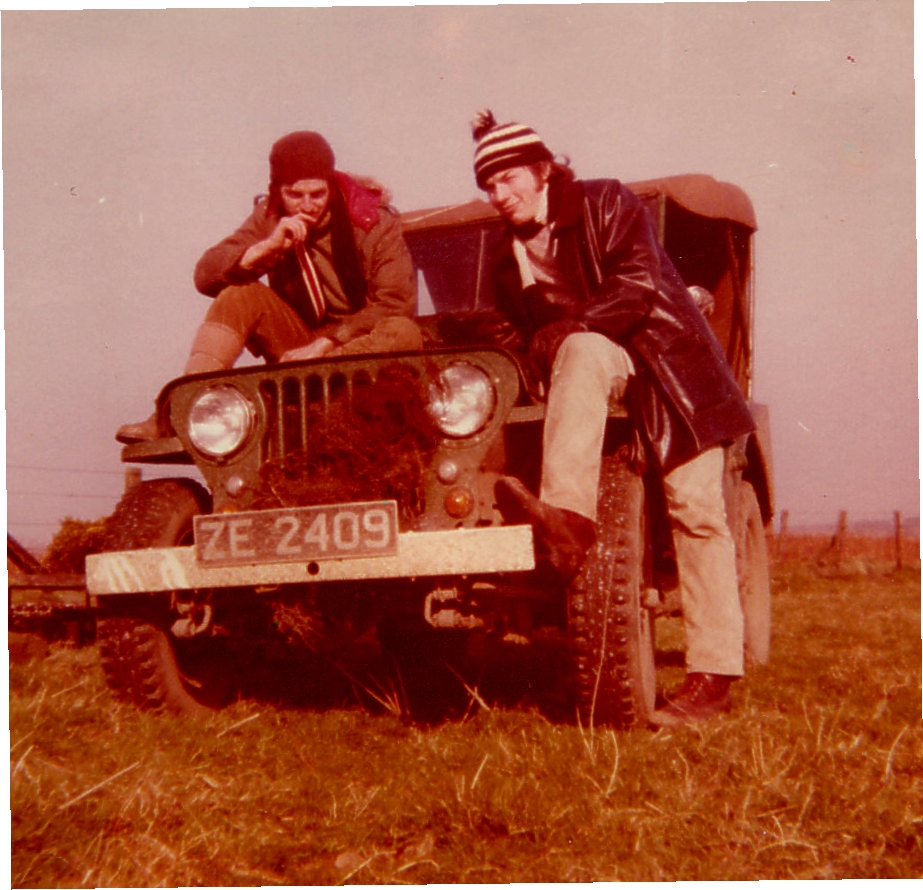 A man and a woman sitting on a motorcycle - Pistonheads - In this sepia tone photograph, two individuals are enjoying a moment in a field. A person is comfortably seated on the hood of an old jeep, which stands prominently in the middle of the frame. Another person stands on the other side of the vehicle, adding a dynamic element to the composition. Both subjects are dressed in attire that suggests a cold or outdoor setting, complete with hats and coats. The juxtaposition of their modern, relaxed poses against the backdrop of a classic vehicle creates a sense of timelessness.