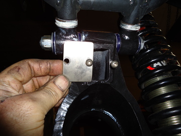 A person holding a cell phone in their hand - Pistonheads - The image shows a close-up of two hands holding a metal bracket with a bolt and washer attached to a piece of machinery. This machinery is geared with black coated components, and there appears to be a red label on one of the components. One of the hands is holding the bracket securely, allowing for the inspection or alignment of the mount. The setting suggests a workshop or installation area, where mechanical work is being carried out.