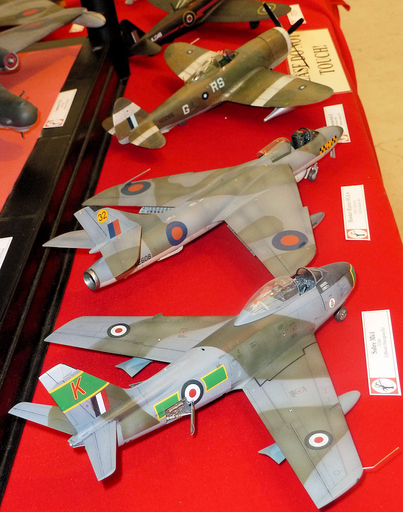 Cosford Pistonheads Model April Raf - The image captures a display of three model planes on a red surface. The planes, demonstrating varying degrees of design complexity and color schemes, are arranged parallel to each other. Each plane bears a number and a label, perhaps indicating their origin, model type, or entry in a model contest. The focus of the image is on the detailing of the models, which harks back to historical aviation designs.