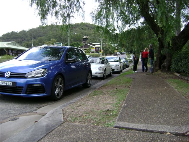 Heavy Ferry Wisemans Pistonheads - In the image, there's a dark blue-colored Volkswagen hatchback parked on the side of a road. This hatchback, which is the main subject of the picture, is accompanied by several other parked cars in the background. The scene takes place on a street lined with trees and grassy areas, adding a touch of greenery to the urban setting. There are also a few individuals visible at a distance, suggesting that this might be a populated area. The cars are parked in front of a building, indicating that the parked cars might belong to people visiting the nearby establishment.