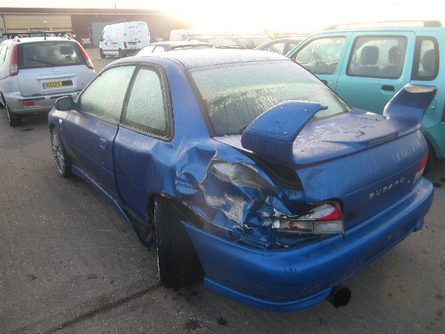 Pistonheads - The image captures a scene of two cars in a parking lot. The central focus is on a blue car, which has been severely damaged on its side. A large portion of the car's side is crushed and bent, as if from a powerful force. The car's taillight is also noticeably damaged. The number plate of the blue car reads "B05 RK". The next car, a green SUV, is partially visible in the background. The positioning of the cars and their relative sizes suggest that the green SUV was probably parked nearby. The incident seems to have taken place in a parking area, as indicated by the presence of other parked cars in the background. The image does not include any people.