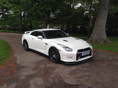 Our Cars - Page 131 - Scotland - PistonHeads - The image shows a white sports car parked on a gravel pathway. The car appears to be a Nissan GT-R, judging by its distinctive design and badge. Its sleek white exterior contrasts with the brown, earthen tones of the ground it's parked on. In the background, there is a line of trees and a grassy area, suggesting the car is in a park or natural setting. The sky above is cloudy, casting a soft light over the scene.