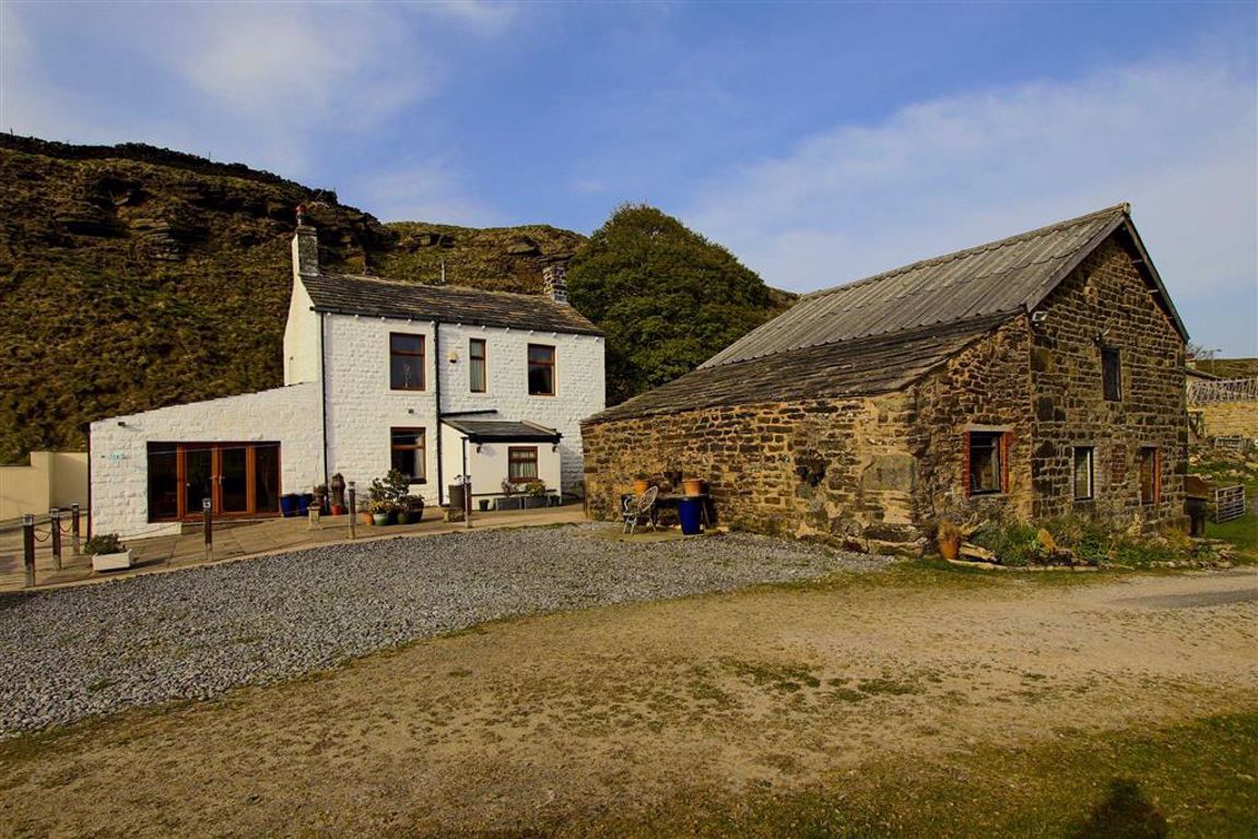 Renovating an old farmhouse and living on the Pennines - Page 1 - Homes, Gardens and DIY - PistonHeads UK - The image shows a rural scene featuring a quaint, stone cottage with a thatched roof. It is situated in a field near an old-looking barn, which has a similar thatched roof design. The cottage and barn are surrounded by open land, indicative of a countryside setting. In the background, there are mountains, adding to the scenic nature of the landscape. The sky is partly cloudy, suggesting it might be late afternoon or early evening. There is no text present in the image.