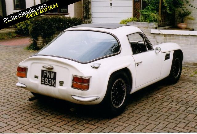 Early TVR Pictures - Page 43 - Classics - PistonHeads - The image features a classic white Piston Heads Speed Matters sports car parked on a brick driveway. The car is an FNM 593K model, distinguished by its distinctive emblem and design elements. The car is rotated to the left, showing its front end and part of the side. The brick driveway surrounding the car is an interesting contrast to its shiny white exterior. The white walls and greenery of potted plants in the background provide a serene setting to this display of automotive beauty.