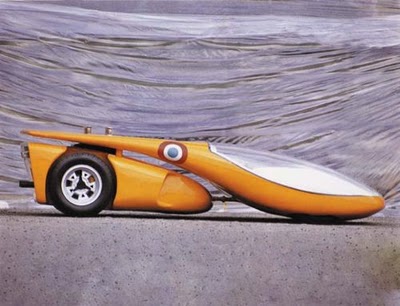 Pistonheads Miura Luigi Lamborghini Colani Concept Lemans - The image captures a unique racing vehicle, which resembles an orange and white cheetah lounging on the floor, positioned in the center. The vehicle has a distinct, elongated design with a single large wheel at the front and a smaller one at the back. The front end of the vehicle features a transparent panel, revealing an engine and other internal components. The backdrop appears to be a gray surface, possibly a floor or a track, with a curtain-like pattern behind the vehicle, adding an element of depth to the image.