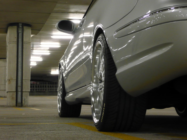 Show us your Mercedes! - Page 8 - Mercedes - PistonHeads - The image shows the rear view of a silver sedan parked inside a garage. The car's body glistens with a polished, reflective sheen, suggesting it is well-maintained. The vehicle's tires are prominently displayed, with the model clearly visible on the rim. The wheels have a five-point star design, indicating the model of the car. The garage has simple support columns and a concrete floor, with a yellow line running along the edge, likely to indicate the pedestrian zone.