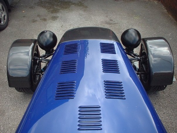 Caterham Blue vs. Viper Blue vs. Kingfisher Blue . . .  - Page 1 - Caterham - PistonHeads - This image captures a scene from the rear end of a blue car, where we can see the back bumper and two rear wheels. The car appears to have a mossy texture on the surface, indicating it might be an older model or has been well used. The wheels are painted black and feature a gold center, adding a contrasting element to the overall blue color of the vehicle. The car lacks any logo or text visible in this image, and no license plate or registration details are present. The vehicle seems to be stationary, as there are no other objects or vehicles in the immediate vicinity of the car.