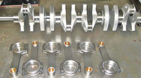 Pistonheads - The image shows an industrial setting with a focus on a collection of precision gears and gear components resting on a floor or workbench. These gears are in various stages of assembly or disassembly, with some connected in tandem and others isolated in pairs. The image suggests a workshop environment, possibly for the assembly, repair, or testing of mechanical devices where such these gears are crucial components. The background is out of focus, emphasizing the gears in the foreground.