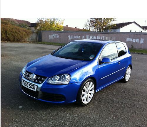 Headache Pistonheads Searching Days Choosing - The image shows a blue Vauxhall Corsa parked on an asphalt surface with a graffit-covered fence in the background. The car's registration plate is clearly visible. The exterior is gleaming, suggesting it is clean and well-maintained. The setting appears to be an open parking lot or possibly the side of a street.