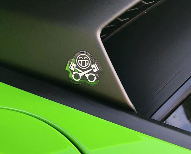 Gel Smiley as seen on PH Instagram - Page 1 - PH Shop - PistonHeads - The image features a close-up of a car's side, focusing on the rear door. The door is painted in a vibrant green color, giving it a sleek appearance. On the side of the car, there's a small logo of a smiling face, which could potentially be an emblem or the logo of the car company. The side door of the car is partially open, revealing the interior light and suggesting an open car door. The sunlight reflects off the green paint, making the door shine brightly.