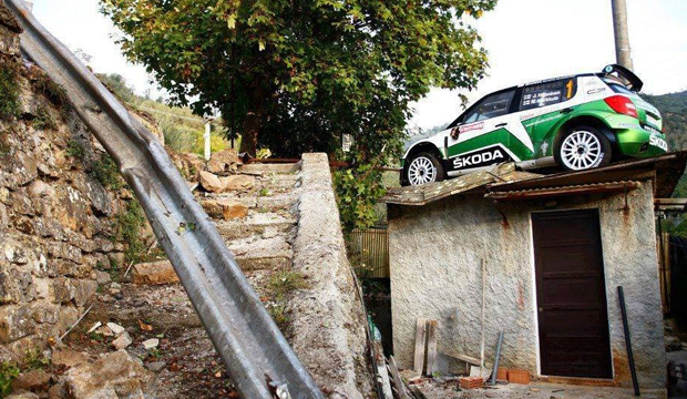 Spot the obvious defect - Page 4 - The Lounge - PistonHeads - The image shows a striking scene where a small green and white Skoda car is parked atop a dirt building or shed. The car's height makes it look like it's on its way to the 'moon'. The car is positioned precariously on a makeshift ramp made of cement blocks. To the left of the car, a large silver-colored metal pipe is visible, which adds to the improvised and daring nature of the scene. The backdrop features a rock wall with green foliage, suggesting this setting is probably in a rural or semi-urban area.