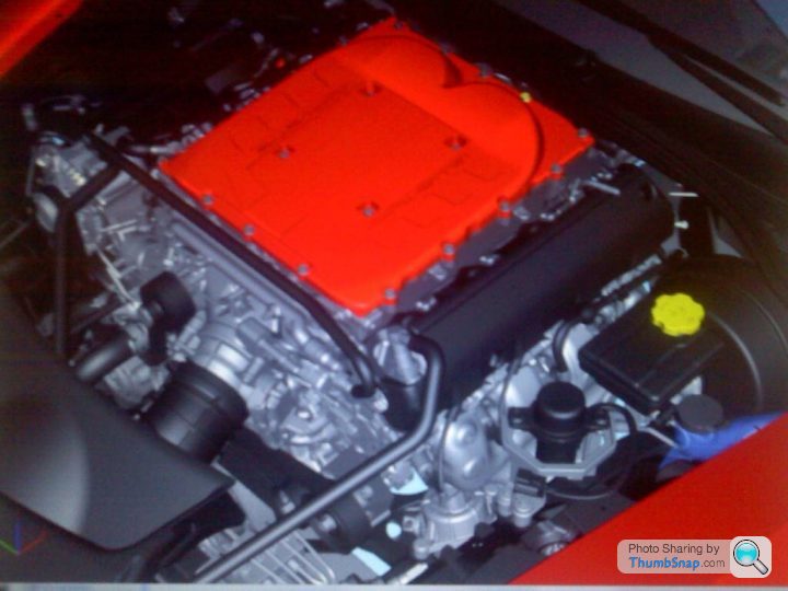 The LT1 is back.....without optispark this time - Page 1 - Corvettes - PistonHeads - The image provides a detailed view of a red sports car engine. At the center of the frame is a metallic engine housing with components like connectors and various metal parts. Hoses, likely for cooling or fluid transport, are visible surrounding parts of the engine. The engine housing appears to be an integral part of the engine, with a robust, textured surface to withstand the high temperatures and pressures associated with engine operation. The picturesque image stirs curiosity about the car's performance and the complexity of the machine.