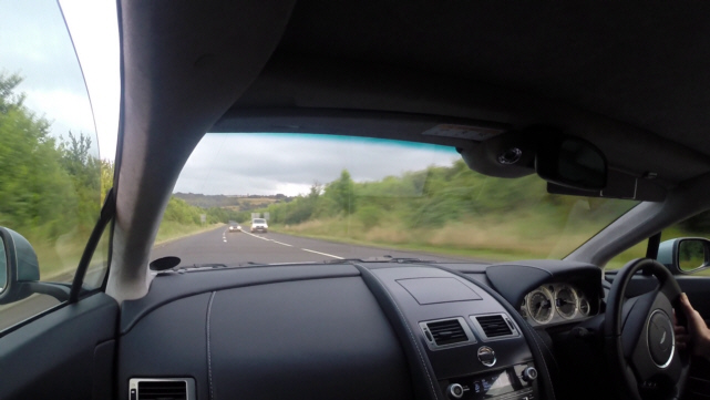 ARE THESE POOR LANE MARKINGS? - Page 1 - Advanced Driving - PistonHeads - The image shows the interior of a car, viewed from the passenger seat. The vehicle appears to be in motion, as indicated by the out-of-focus scene through the windshield. There are no visible people in the car. The dashboard and various controls, such as the infotainment system and air vents, are within the frame. The atmosphere suggests a journey on an open road.