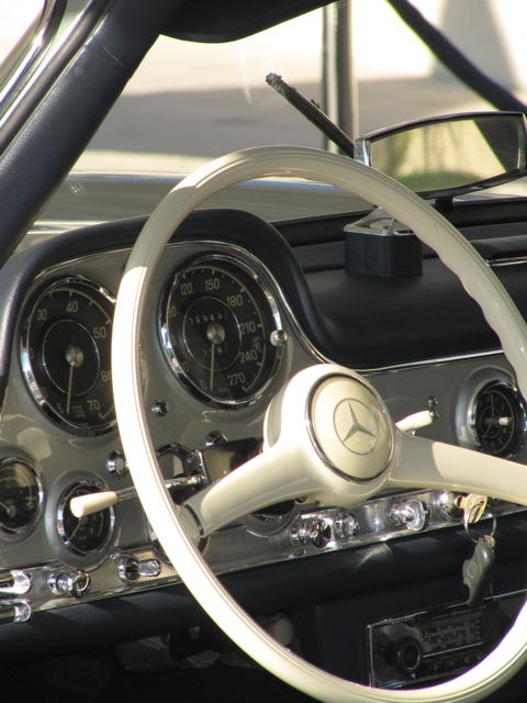 Pistonheads Classic Emaar - The image captures the interior of a vintage car, focusing on the driver's side. Dominating the frame is the steering wheel, which features a silver and white Mercedes emblem in the center. The dashboard and control panel, bathed in a dark, vintage finish, are adorned with a multitude of gauges and a cluster of knobs and dials, indicative of the pre-digital era of automotive design. The car's interior architecture and details suggest it's a classic model that exudes a sense of nostalgia. The image offers a glimpse into the past, providing a tangible connection to automotive history.