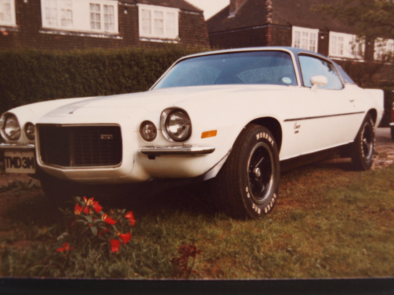 Lets see a picture of your classic(s) - Page 220 - Classic Cars and Yesterday's Heroes - PistonHeads - The image captures a scene of a classic white sports car parked on a grassy area. The car, distinguished by its retro design, features a prominent white front bumper and a black Soft Top roof. It's complete with silver alloy wheels and a black fabric interior, adding to its vintage charm. The car is parked in front of a building, with a neatly maintained green lawn and a small clump of red flowers, adding a touch of nature to the urban setting. A license plate reading "M29" is prominently visible on the front of the car, suggesting it's ready for a drive around town.