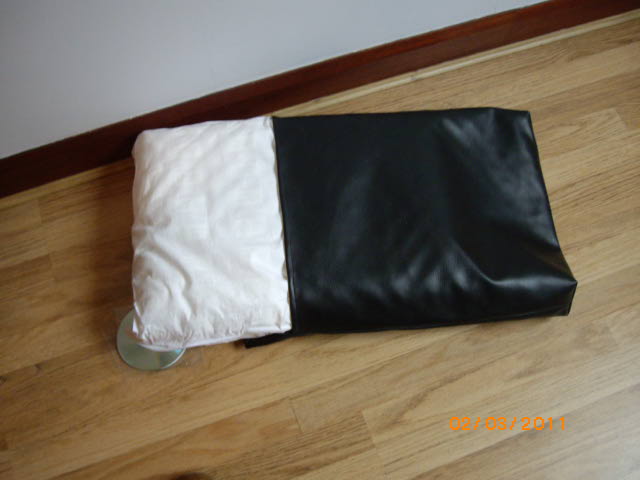 Pistonheads - The image depicts a black leather object, which appears to be resembling an enveloped package, laying on a wooden floor next to what seems like a cream-colored object or pillow. The contrast between the smooth, shiny leather and the grainy texture of the wood is striking. No text is visible in the image, focusing solely on the objects and their arrangement on the floor. The photo is taken from an elevated angle, providing a clear view of the items on the wooden surface.