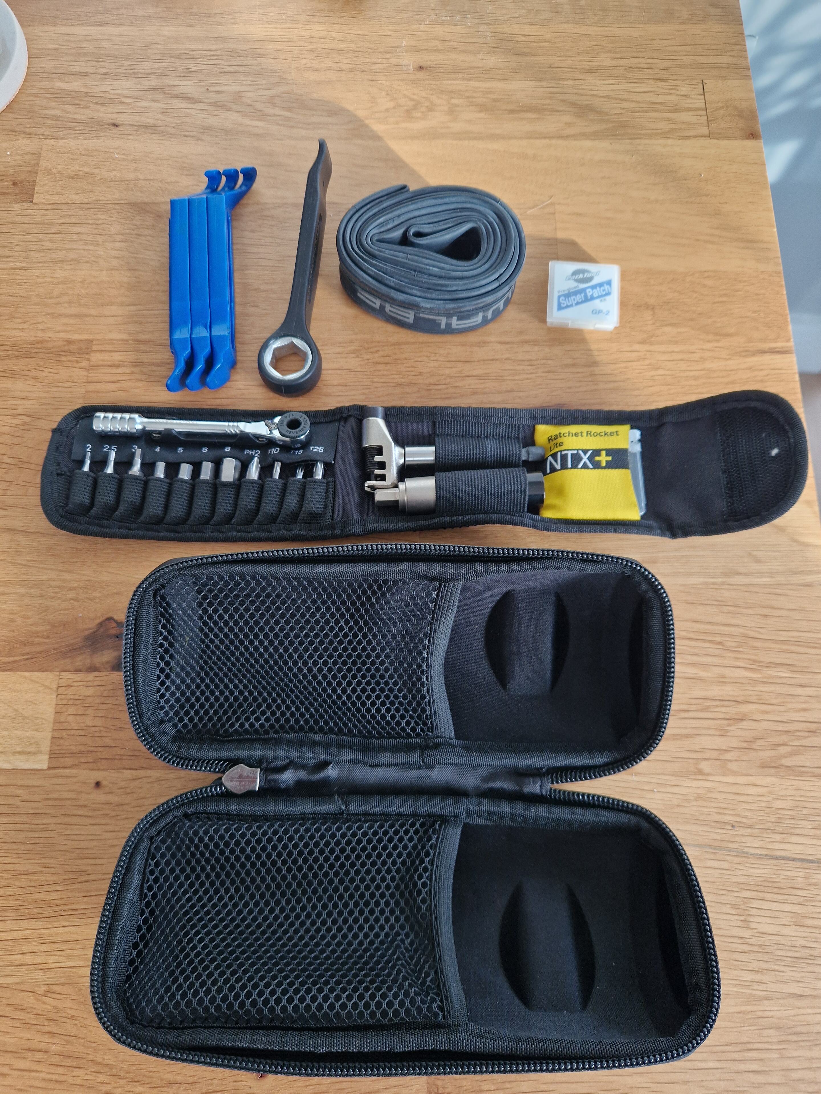 Pistonheads - The image shows a small, black tool kit with an open lid displayed on a table. Inside the case, there are various tools including a screwdriver and a pair of pliers. To the right of the tool kit, there is a coil of wire, along with some additional tools which are partially obscured. The scene suggests that someone may be preparing to fix or work on something mechanical or electrical.
