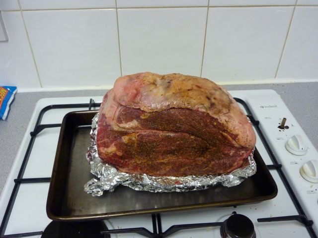 The bbq photo & recipe thread - Page 74 - Food, Drink & Restaurants - PistonHeads - The image shows a whole, raw roast covered in aluminum foil, resting atop a stove. The roast appears to be of a large size, occupying the entire pan. The stove is a gas model with a white stovetop and black burners, and the oven door with its visible weight scale adds a unique detail to the domestic setting. The aluminum foil covers the roast, reflecting its weight, indicating that it is being weighed.