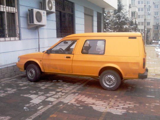 Chinese Pistonheads Content Heres Maestro - The image shows a bright yellow car parked on a bricked driveway. The car is facing towards the right side of the image. The driveway is neatly paved with bricks, and a building with a white facade forms part of the background. A metal railing can be seen in front of the car, possibly for added security or as a parking stop. Additionally, there are two air conditioning units affixed to the wall of the building behind the car, suggesting that the building may have been used for commercial purposes.