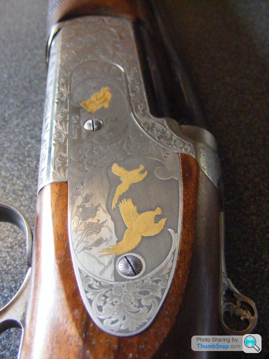 The PH Gun Cabinet - Shooting Matters - Page 10 - Sports - PistonHeads - The image showcases a close-up view of a rifle, prominently highlighting its decorative barrel. The barrel is adorned with intricate engraving featuring two birds and a background pattern, suggesting craftsmanship and perhaps artistic significance. The rifle is side-loaded and has a classic design, featuring a wooden stock and a metallic frame. An inscription indicating the barrel's number is discernible, indicating its uniqueness.