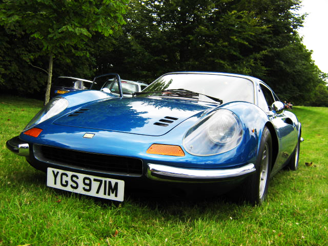 Motors Pistonheads Manor - The image shows a blue car parked on what appears to be a grassy field. The car is a Porsche, identifiable by the sports car's characteristic rounded front bodywork, which contrasts with the sleek lines of the vehicle. The car is adorned with a distinctive black stripe running along the side, a feature commonly found in high-performance models. Additionally, the car has yellow headlights and a black grille, adding to its sporty aesthetic.

The car is the central focus of the image, with the grassy field and other cars hinting at an outdoor event or parking lot. In the distance, the tops of trees can be seen, providing a rural or semi-rural setting for the vehicles. The license plate of the blue car is also visible, but it's not necessary to include it in the description. Overall, the image conveys a sense of elegance and luxury associated with the Porsche sportscar.