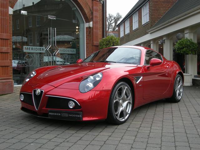 Wedding car ideas - Page 1 - East Anglia - PistonHeads - The image captures a sleek red Maserati sports car parked on a brick sidewalk in front of a store or restaurant named "Meridien Meredden." The car's polished exterior reflects the overcast sky above and it is positioned in what appears to be a European urban setting where classic red brick buildings line the street. The sports car exudes an air of elegance and luxury.