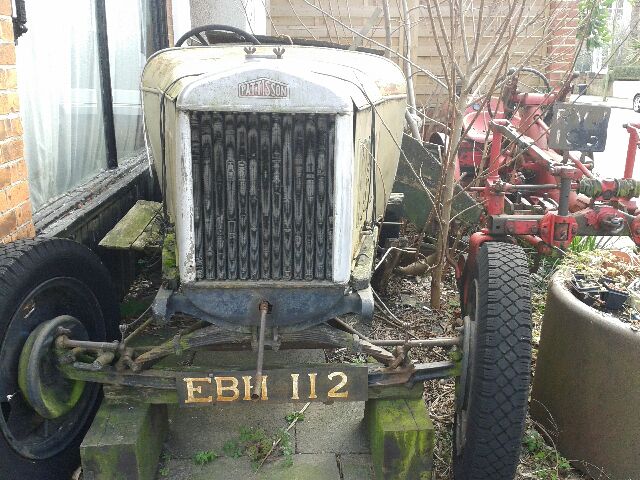 Classics left to die/rotting pics - Page 442 - Classic Cars and Yesterday's Heroes - PistonHeads - The image showcases a vintage tractor, parked and partially obscured by a mossy tree and other outdoor items. Its registration number is clearly visible, indicating it's still in use. The tractor appears to be the main focus of the image, as it is central and partially highlighted against the background. The surrounding wreckage and plants suggest a sense of disuse and perhaps a need for restoration.