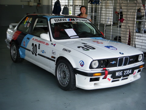 Pistonheads Afos Sepang - The image portrays a BMW car, prominently featuring a number 30, displayed indoors within a showroom-like setting. The car is predominantly white with blue accents. Along with a logo that reads "BMW power," the car is adorned with multiple stickers and a license plate reading "WE 2354." The car appears to be meticulously maintained, indicative of its status as a show car. To the left of the car, a person can be seen, possibly an attendant or potential customer, providing a sense of scale to the vehicle.