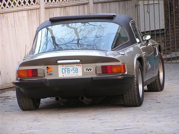 Early TVR Pictures - Page 90 - Classics - PistonHeads - In the image, a classic Silver VW Beetle is parked on a gray pavement. The car's license plate, reading "CFB-58", is clearly visible. The vehicle's ornate headlights and the silver and black color scheme give it a distinctive and vintage look. The car is positioned in front of a white fence, which contrasts with the parked car. The scene doesn't feature any people or moving objects, giving a calm and static impression.