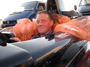 Living Racing Pistonheads Ocd - In the image, a man is seen in a car seat, appearing to be in a vehicle. He is surrounded by various items, including a black bag and a red bag, and there's text on the red bag that says "Lincoln". The man seems to be ill or unwell. He has a noticeable flushed face and is resting, suggesting that he might be unwell. The background of the image reveals a parking lot with other vehicles, indicating that the car he is in might be in a public space or a parking area.