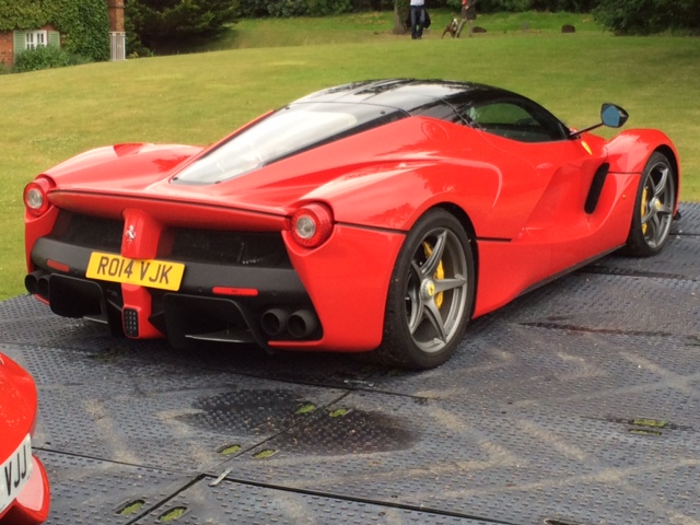 A red car with a surfboard on top of it - Pistonheads - The image showcases a vibrant red Lamborghini sports car parked on a grate surface. The car is facing towards the left side of the image. Its sleek design and shiny surface suggest it is well-maintained. In the background, there are green grass and trees, indicating that the car is parked outdoors. The grate surface on which the car is parked allows for good drainage, as evidenced by a few small puddles visible underneath.