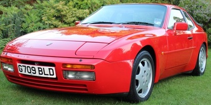 I just bought an 89 944 turbo - Page 1 - Front Engined Porsches - PistonHeads - The image shows a beautiful red sports car parked on grass. The car's front and one of its wheels are clearly visible, and the vehicle's color stands out vibrantly against the background. The other wheel is partially obscured by the car's hood. There is a subtle reflection of the car's shape on the ground, adding a sense of its size. The car seems to be well-maintained, with no significant visible damage. The overall composition of the photo highlights the car in a moment of calm, away from the rush of city life.