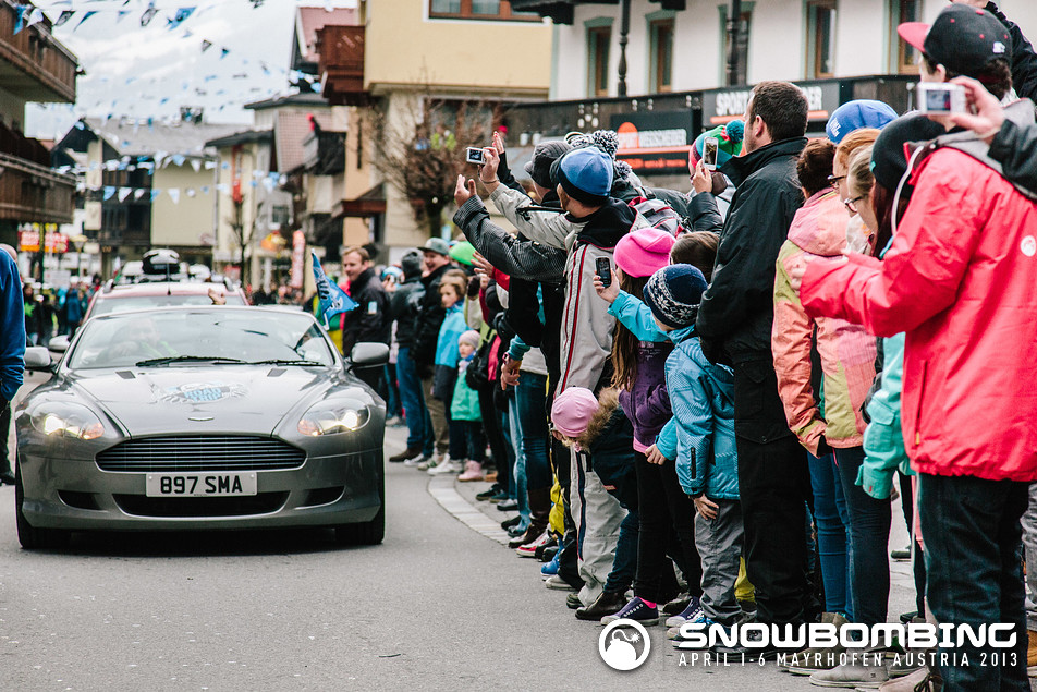 Show us your DB9  - Page 1 - Aston Martin - PistonHeads - The image captures a lively scene of crowds of people lining the side of a street. They are eagerly watching a silver sports car drive by. The car is displaying the number "897 SMA" and seems to be in motion. The crowd appears to be a mix of adults and children, all engrossed in the spectacle. Various individuals in the crowd are holding up their devices, possibly capturing photos or videos of the passing car or simply live-streaming the event. The setting suggests this might be a special event, like a parade or public exhibition, where such car shows can be common.