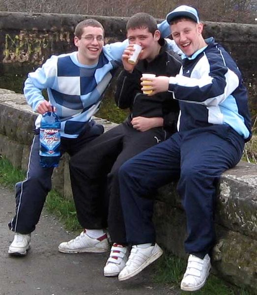 Durham Fiat - is it really that bad? - Page 1 - General Gassing - PistonHeads - This image captures a jovial scene of three young men sharing a moment of camaraderie. They are casually dressed, wearing sunglasses and sportswear, suggesting a relaxed, outdoor setting. The boy on the left is holding a blue drink and smiling broadly, while the two on the right are seated on a stone ledge, also smiling and one raising a toast with his drink. Their poses indicate a sense of fun and togetherness. The setting appears to be a public park or path, with a visible wall in the background.