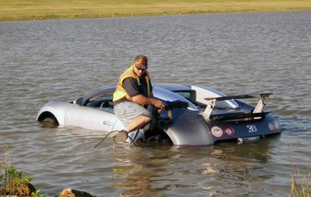 The camera can capture some fantastic moments IV - Page 376 - Photography & Video - PistonHeads - The image features a person working diligently in murky floodwaters, trying to open the trunk of a marooned car submerged in a lake. The car is partially flooded, with water reaching just beyond the driver's seat where the person is kneeling. The lake extends into the distance, merging with a grassy area that's visible above the waterline. The individual appears focused on accessing the car's contents, likely guarded by the flooded state of the vehicle.