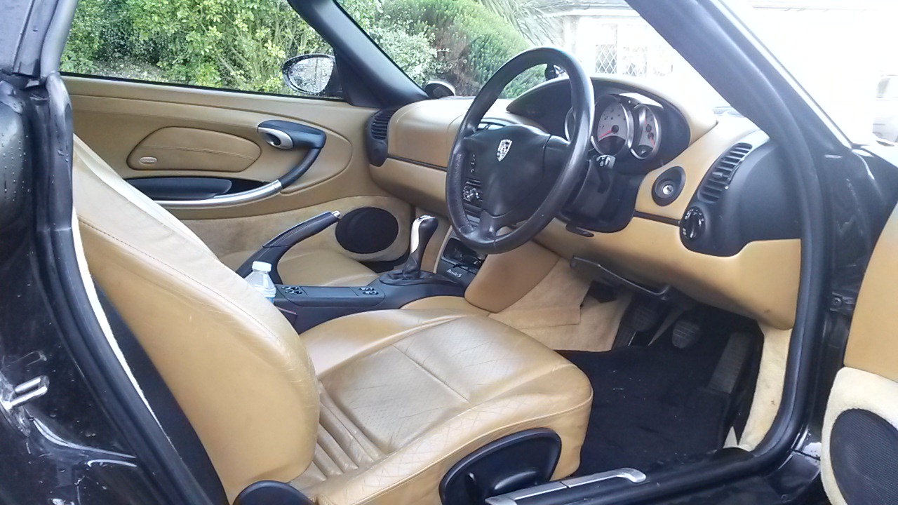 A close up of a car parked in a parking lot - Pistonheads - The image shows the interior of a red car. The driver's seat is visible from the passenger's perspective, with the steering wheel on the right-hand side. The seats appear to be leather, and the vehicle appears to be older in style. The rear seats of a car are visible, and there's a hand rail for passengers to hold onto.