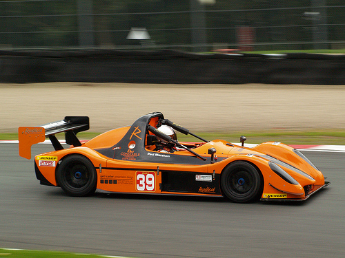 A red motorcycle is parked in a parking lot - Pistonheads - The image captures a dynamic scene of a race car, in the distinctive shade of orange, speeding along a racetrack. The car is adorned with the number 39 on its side and has a single white stripe running down its middle. In the cockpit, a driver is visible, gripping the steering wheel and navigating the vehicle along the track. Any advertisements or branding are blurred, adding to the sense of speed and movement. The corner of the track is marked by a curb, providing a visual guide for the driver as they navigate the curve.