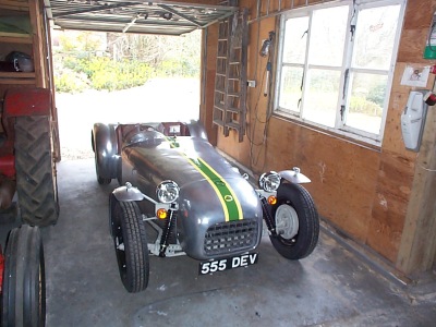 Pistonheads - The image showcases a silver and yellow one-wheel car, also known as a sidecar, parked in a garage or storage area. The car is displaying the registration plate "55 DEV", indicating its unique identity. The interior of the storage area features visible construction elements, including corrugated metal sheets above and metal pipes on the side. On the left side of the frame, there seems to be some agricultural equipment, suggesting the location might be a farm or a workshop specializing in tractors or vehicles. The overall scene portrays a blend of vintage transportation and industrial machinery.