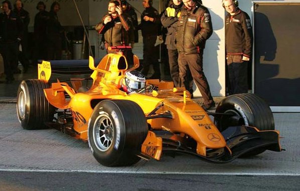 A man standing next to a red and white motorcycle - Pistonheads - The image shows a vibrant orange Formula 1 car on a track, ready for action. In the foreground, there is a person standing beside the car, likely a driver or team member, wearing a helmet and holding a microphone, suggesting they might be communicating with the team or the audience. Behind the car, there is a group of individuals, presumably team members or support staff, observing the person with the microphone. They seem to be dressed in casual attire with some wearing jackets with patches on the sleeves, which might indicate their roles within the F1 team. The setting suggests an active track environment, with the focus on the driver preparing for the race.