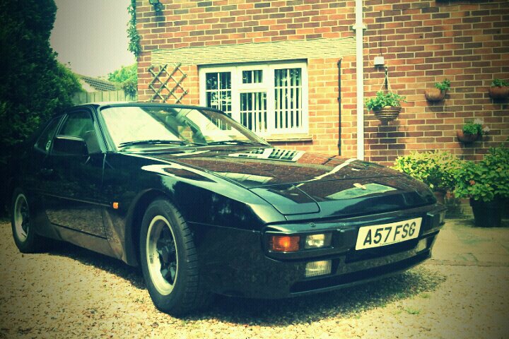 Pistonheads Love Hate - The image shows a black sports car parked in front of a well-manicured house. The car is sleek with black trim detailing its design. It's sitting on a pebbled driveway, and the house behind it has numerous planters with plants, contributing to a maintained and elegant exterior. The image has an editorial quality, often used in car reviews or advertising, with a focus on the vivid vehicle and the charming house.