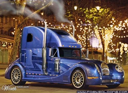 Colors Pistonheads Crazy - The image features a large, colorful truck parked at night in a festive setting. The truck has a shimmering metallic blue exterior, adorned with chrome accents and geometric designs that reflect the city lights. The cab of the truck is blue, matching the rest of the vehicle, while the flatbed is painted in white and green, adding to the overall vibrant design theme. The truck is equipped with a fat cat's nose hood, giving it a unique and personified appearance. The backdrop consists of beautifully decorated Christmas trees lit up with lights, enhancing the festive ambiance.