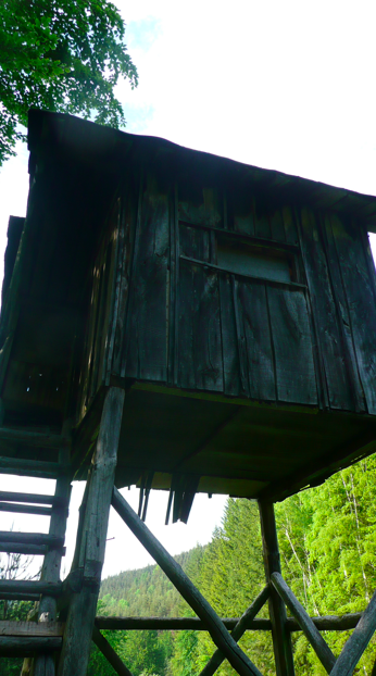 Little overnight trip to the Balkan range - Page 1 - Off Road - PistonHeads - This image features a wooden cabin elevated on stilts. The cabin appears old and weathered, with a visible window and a sloping roof. The stilts are strong and sturdy, supporting the structure upward. The setting is a natural environment with visible trees in the background. The sky above is partially cloudy. The overall scene suggests a rustic, outdoor location.