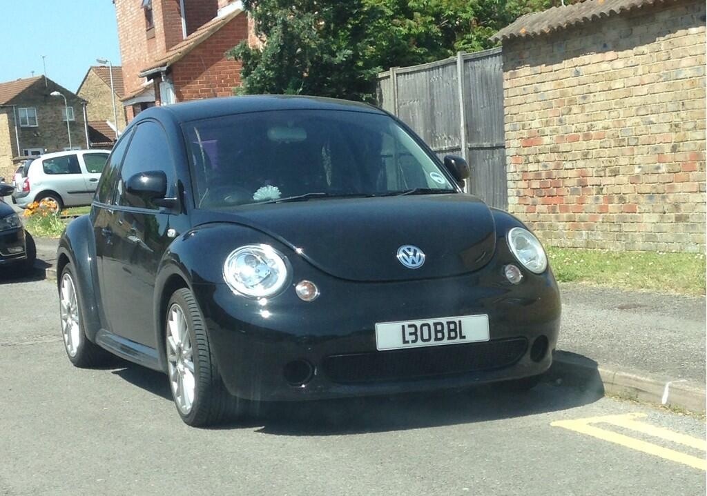 Spacing number plates? Legality? - Page 2 - Speed, Plod & the Law - PistonHeads - The image shows a black Volkswagen Beetle parked on a road next to a brick wall. The vehicle has the volkswagen emblem on the front and a license plate that reads "130BBL". It has two headlights on the front, a luggage rack, and a black soft top convertible roof. In the background, there is a parked car to the left and some greenery visible behind the brick wall. The road appears to be in a residential area.