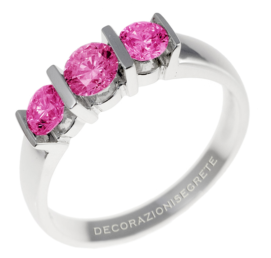 This image shows a piece of jewelry, specifically a ring with a series of gemstones. The primary color of the stones appears to be pink, with some grey accents. The metal looks to be white, possibly silver or white gold, and the ring is designed with multiple prongs to hold the stones in place. The band of the ring has writing on it, which appears to be the brand name "DIAZIONISI EGESTE." The background is plain and does not distract from the ring, which seems to be the sole focus of the image. The lighting is bright and even, suggesting a professional photography setup intended to showcase the piece of jewelry.