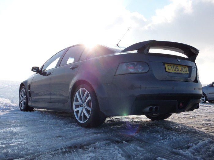 My VXR8 - pics taken today - Page 1 - Readers' Cars - PistonHeads - The image shows a black sedan car parked on what looks like a snowy surface. The car is a modern design with a sporty rear wing. The rear lights and registration tag are visible, and the car features alloy wheels. The surrounding environment suggests a clear sky with a hint of sunlight, as indicated by the lens flare effect over the car. The ground appears to be partially covered in snow, contributing to a wintry or cold atmosphere.