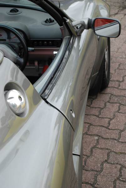 Service Pistonheads Sunday - The image showcases a close-up view of a silver car featuring a streamlined design. The focus of the image is on the car's door, which is visible through the side mirror. The mirror is attached to the side of the door frame, providing a reflection of the surrounding area, including a section of brick pavement. The door itself has a door handle, reflecting the car's overall sleek and modern aesthetic. The background is predominantly gray, suggesting an outdoor setting, possibly an urban environment. The overall image conveys a sense of elegance and refinement associated with the car's design.